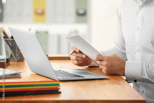 Young man working with laptop and documents in office  closeup