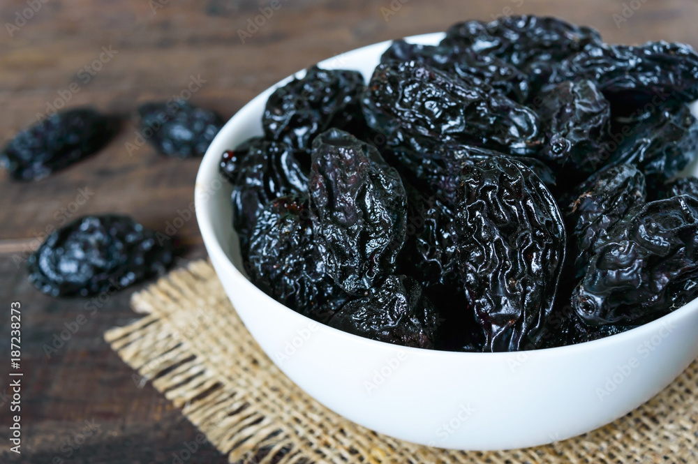 Prunes in a ceramic bowl on a dark wooden background. Dried fruits. Prunes in a ceramic bowl on a dark wooden background. Dried fruits.