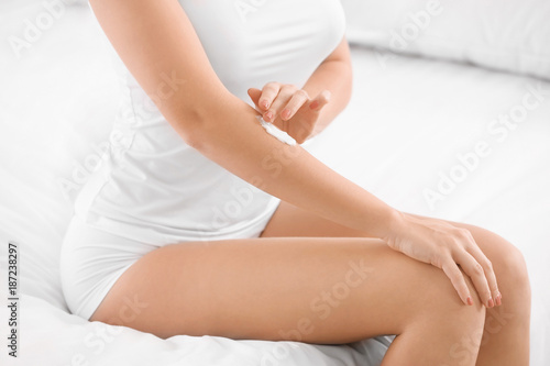 Young woman applying body cream at home, closeup
