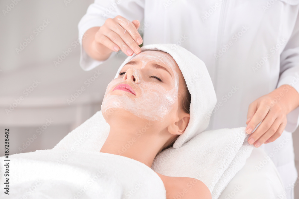 Beautician applying cream onto young woman's face in spa salon Beautician applying cream onto young woman's face in spa salon