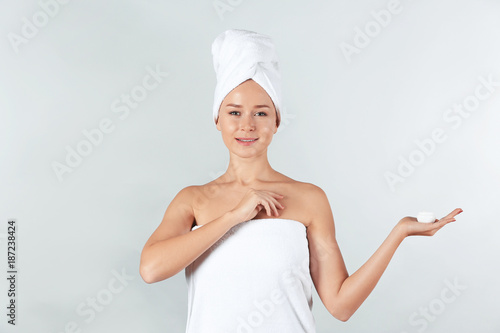 Young woman with body cream on light background