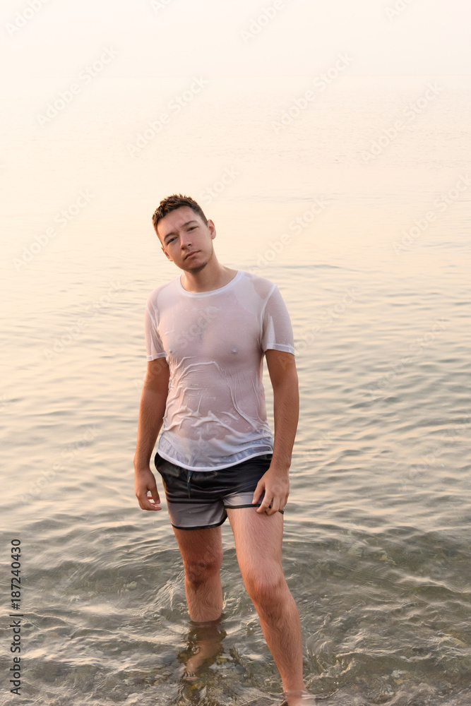 Young man standing in the water in a wet white t-shirt with protruding  nipples Stock Photo | Adobe Stock