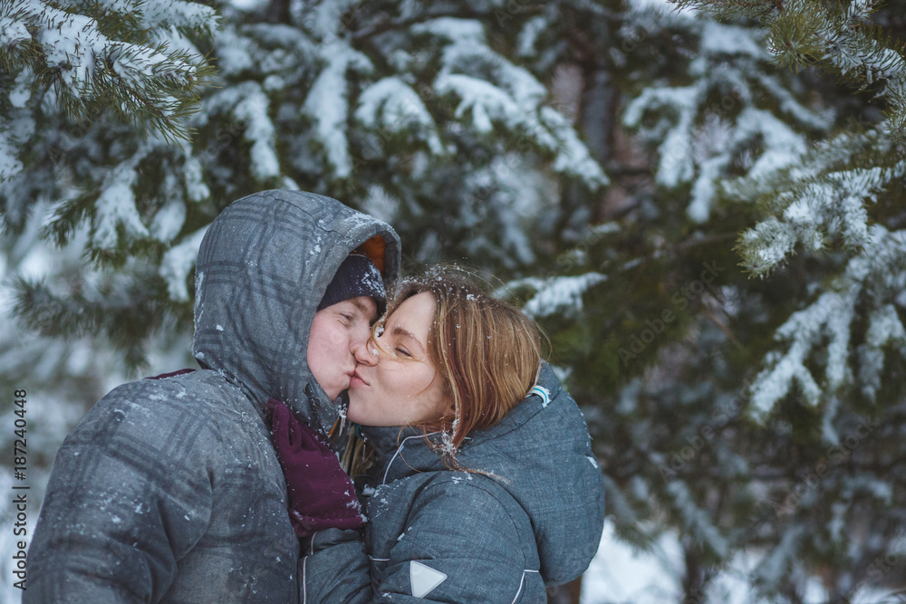 Happy snow covered couple kissing under fir branches in winter forest. Concept healthy romantic holidays on fresh air Happy snow covered couple kissing under fir branches in winter forest. Concept healthy romantic holidays on fresh air