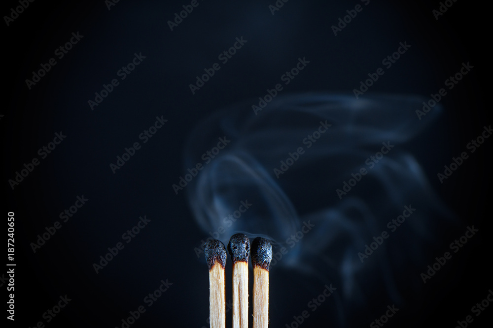 Three matches with burnt heads emitting the last effort of the remnants of smoke on black background