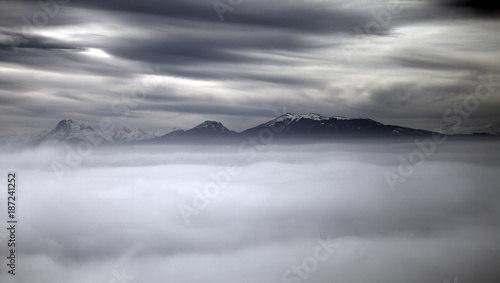 landscape of the countryside and Italian mountains shrouded in fog in autumn, in the background the snow-capped peaks of the mountains, an almost surreal and fantastic atmosphere