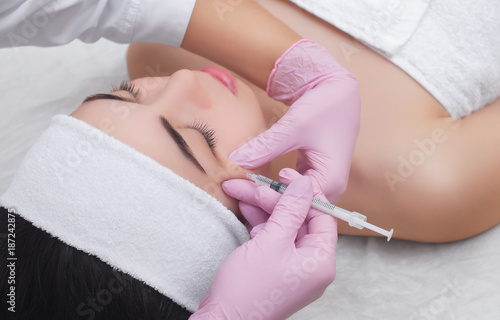The doctor cosmetologist makes the Botulinum Toxin injection procedure for tightening and smoothing wrinkles on the face skin of a beautiful  young woman in a beauty salon.Cosmetology skin care.