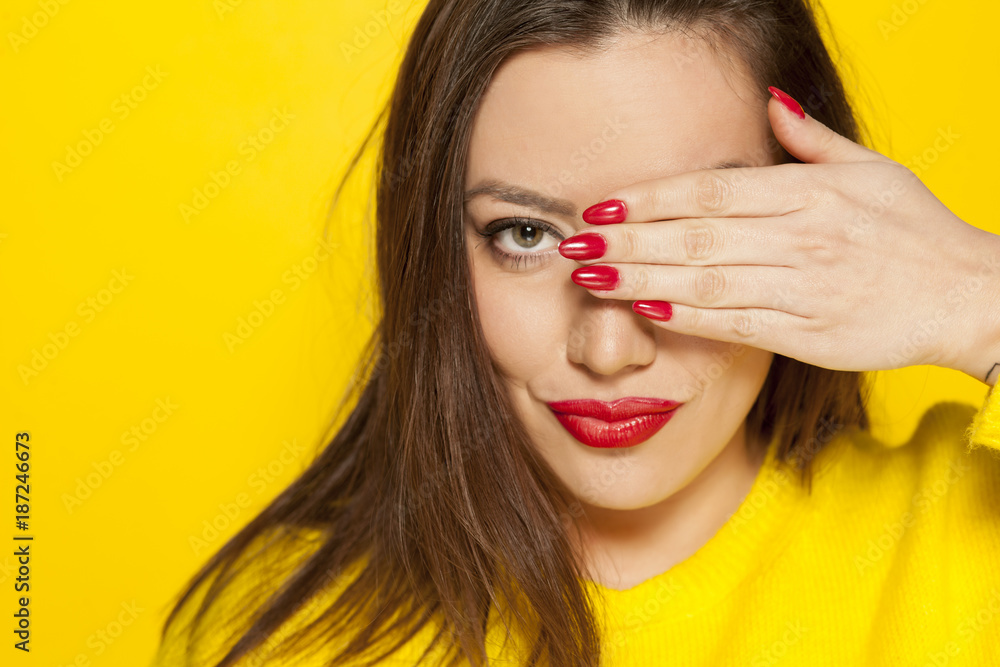 Fototapeta premium beautiful woman in a yellow blouse, covering her eye with her hand on a yellow background