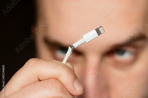 Close up portrait with angry young man who are looking for the white broken smartphone usb cable.