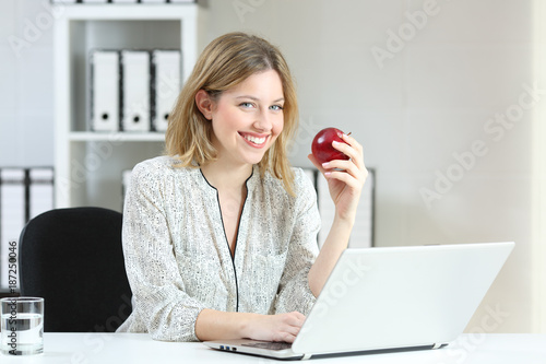 Businesswoman holding an apple looking at you at office