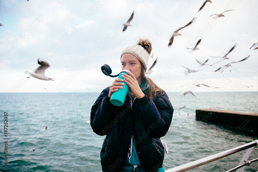 Obraz premium Pretty girl drinking tea from thermos near the sea.