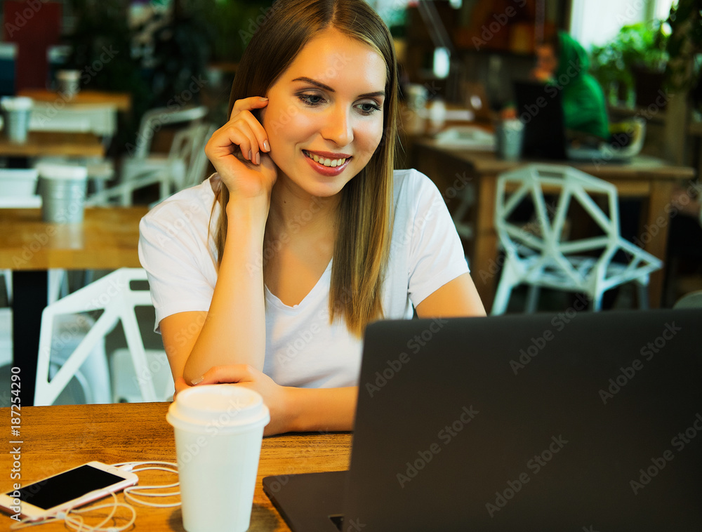 Happy young woman drinking coffee/tea and using laptop  in a cof