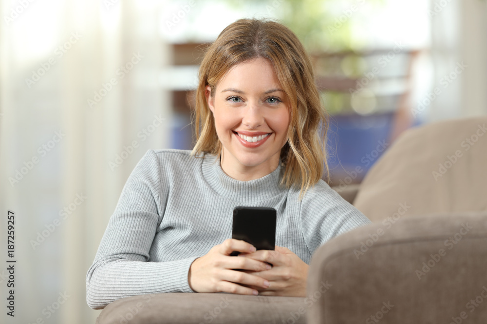 Woman holding a smartphone looking at camera at home Woman holding a smartphone looking at camera at home