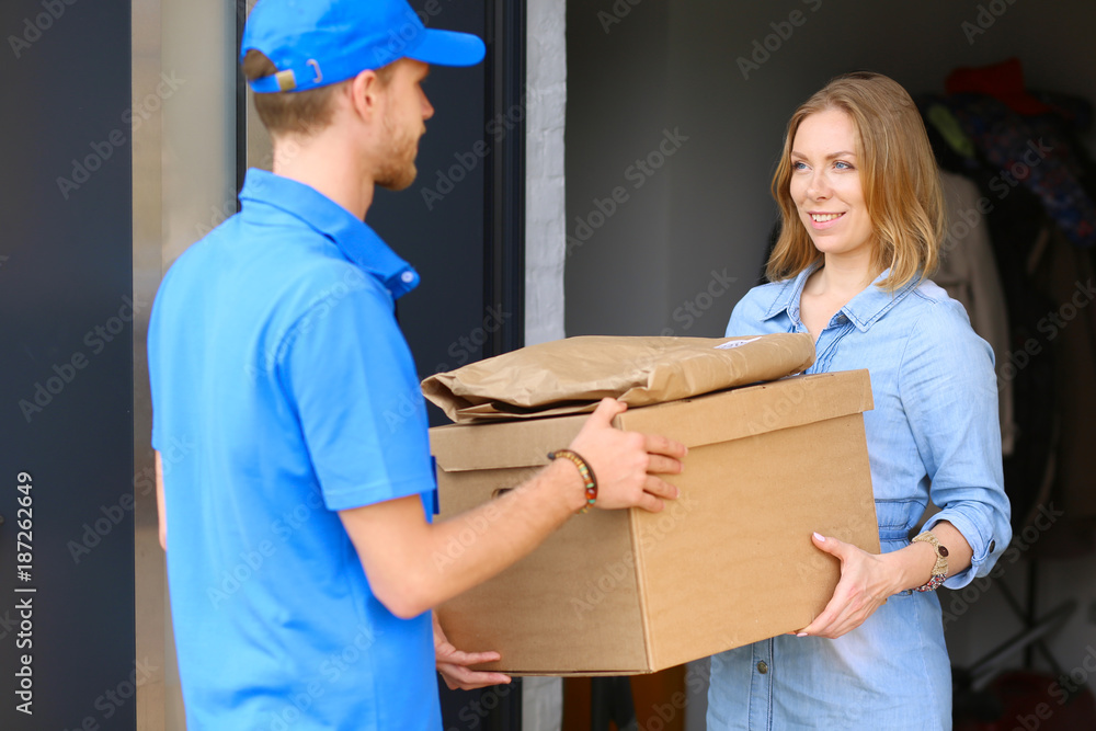Smiling delivery man in blue uniform delivering parcel box to recipient - courier service concept. Smiling delivery man in blue uniform Smiling delivery man in blue uniform delivering parcel box to recipient - courier service concept. Smiling delivery man in blue uniform