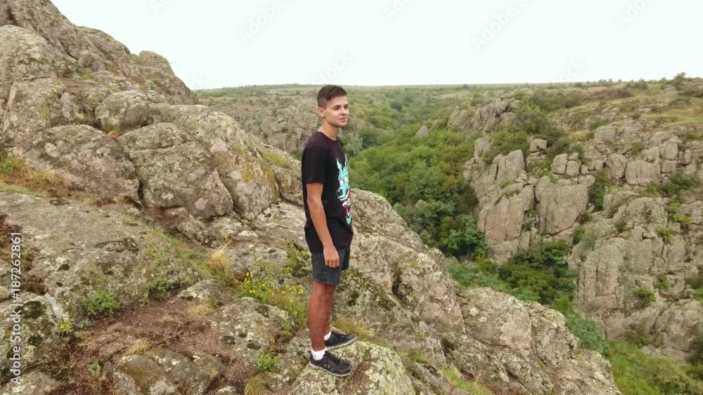An original bird`s eye view of hilly mountains covered with huge brown stones and a young man in a black tshirt and shorts on it An original bird`s eye view of hilly mountains covered with huge brown stones and a young man in a black tshirt and shorts on it