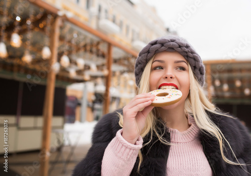 Attractive blonde model bites delicious gingerbread cookie against light decoration at the square in Kiev