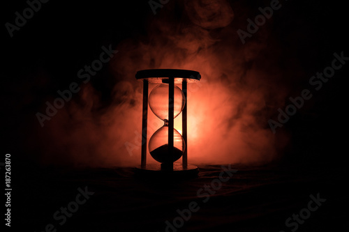 Time concept. Silhouette of Hourglass clock and smoke on dark background with hot yellow orange red blue cold back lighting, or symbols of time