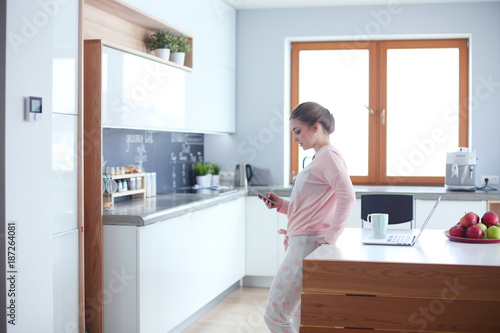 Woman using mobile phone standing in modern kitchen.