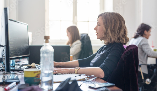 Women in startup business and entrepreneurship. Yound devoted female AI programmers and IT software developers team programming on desktop computer in startup company share office space. photo