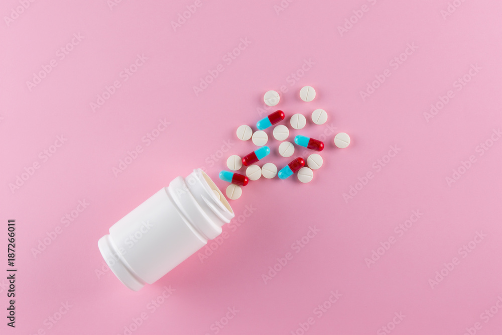 top view white round pills and blue red capsules of medicine spilling