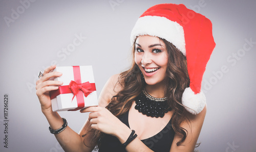 Woman in Santa hat holding gifts, isolated on gray background