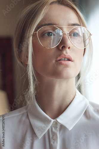Portrait of a beautiful young blonde woman with chic makeup and big fashionable glasses, wears white silk shirt . Adjusted with a touch of charming colors.