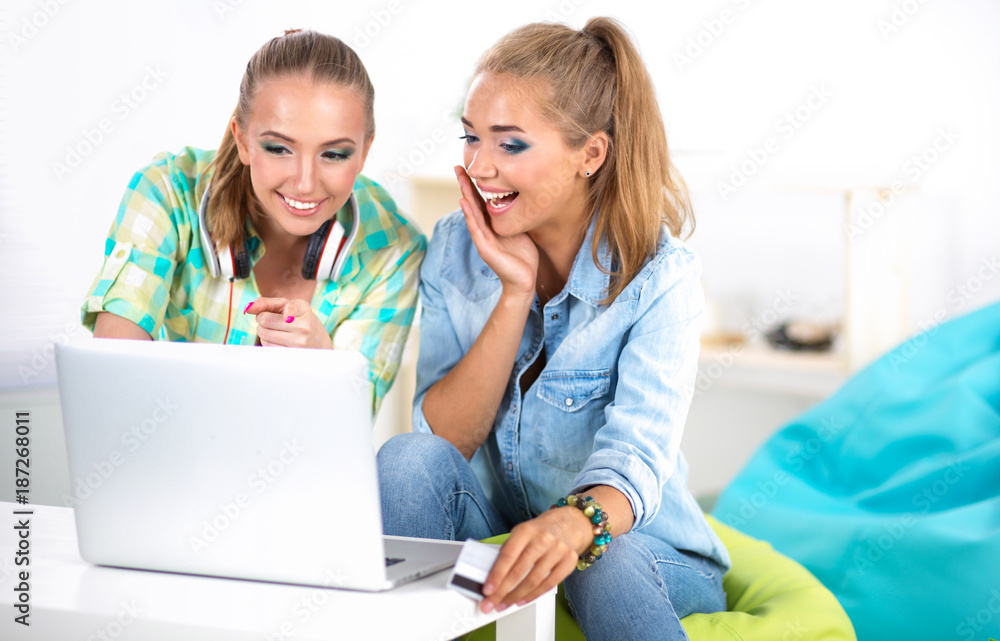 Two young women sitting with laptop and credit cart at home Two young women sitting with laptop and credit cart at home