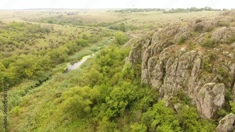 A striking bird`s eye view of a wild looking canyon among high hills, green trees and some narrow river flow on a sunny day in summer. A striking bird`s eye view of a wild looking canyon among high hills, green trees and some narrow river flow on a sunny day in summer.