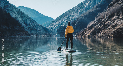 a woman with yellow plumber paddle surfing on a lake in a snowy mountain landscape
