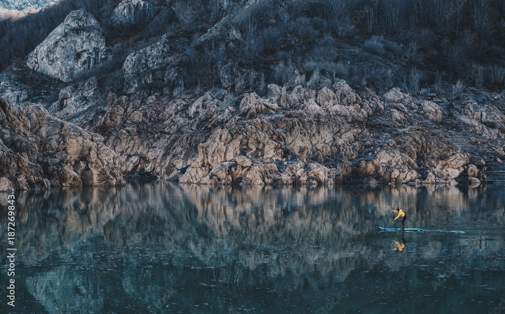 a woman with yellow plumber paddle surfing on a lake in a snowy mountain landscape a woman with yellow plumber paddle surfing on a lake in a snowy mountain landscape