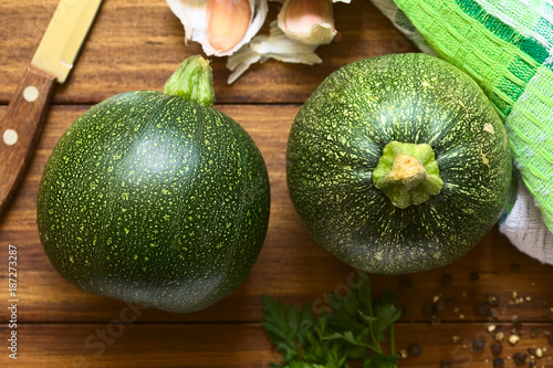 Two raw round zucchinis, parsley and garlic on the side, photographed overhead with natural light (Selective Focus, Focus on the top of the zucchinis)