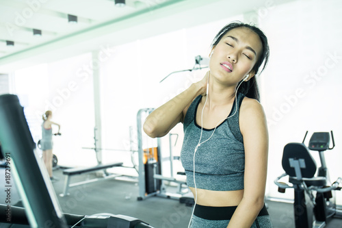 Attractive asian tan female touching her neck and shoulder in pain, Young athletic woman stretching her painful neck and shoulder, healthcare and medical concept.