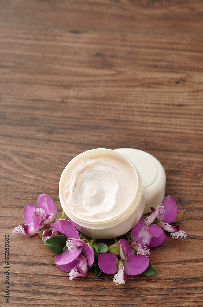 A tub of hand lotion displayed with  small purple flowers