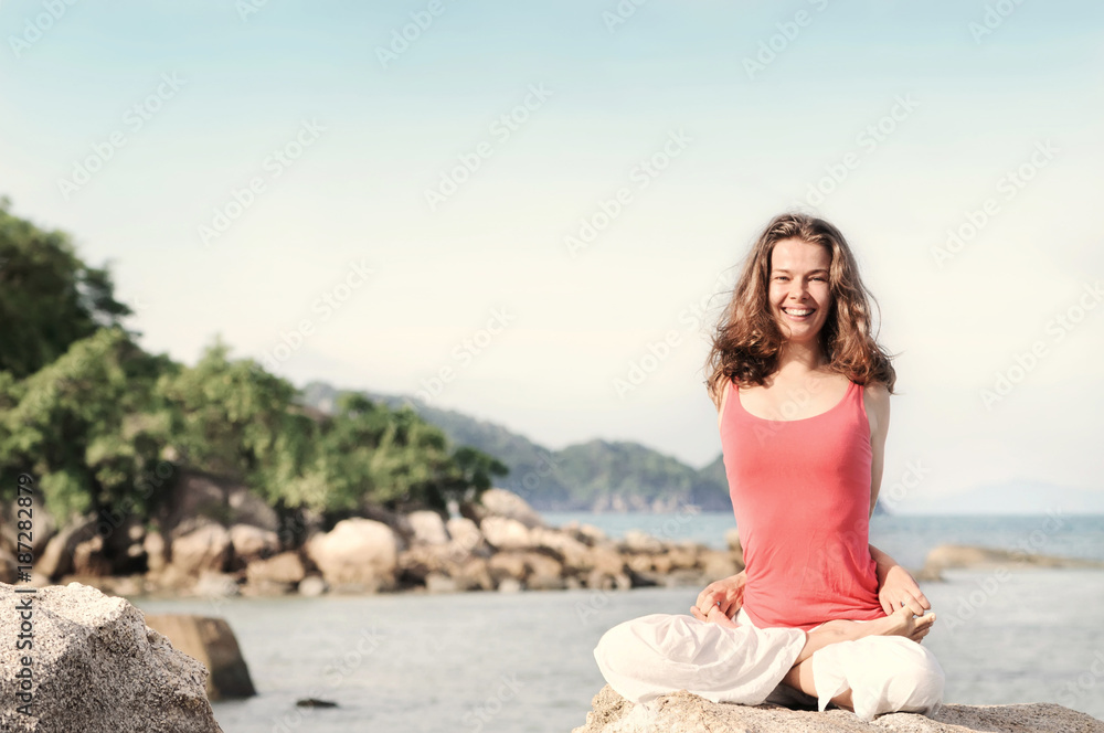 Young woman yoga teacher smiling during morning yoga practice on the beach