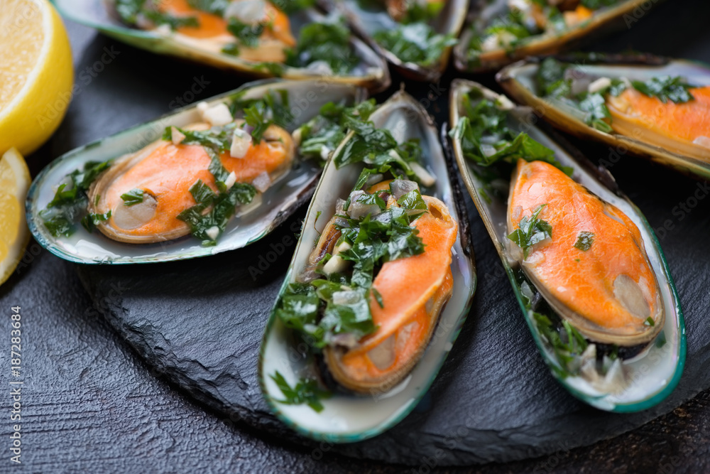 Close-up of boiled green mussels with parsley sauce on a stone slate, selective focus Close-up of boiled green mussels with parsley sauce on a stone slate, selective focus