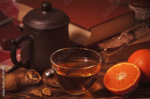 Cup of tea on wooden table with tangerines, walnuts and books
