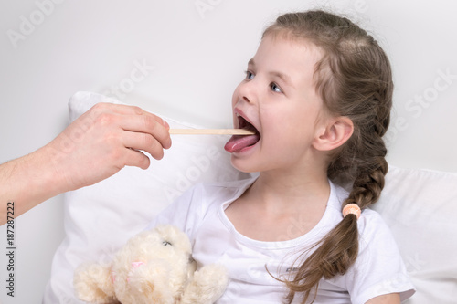 the child looks at the throat with a wooden stick, without getting out of bed photo