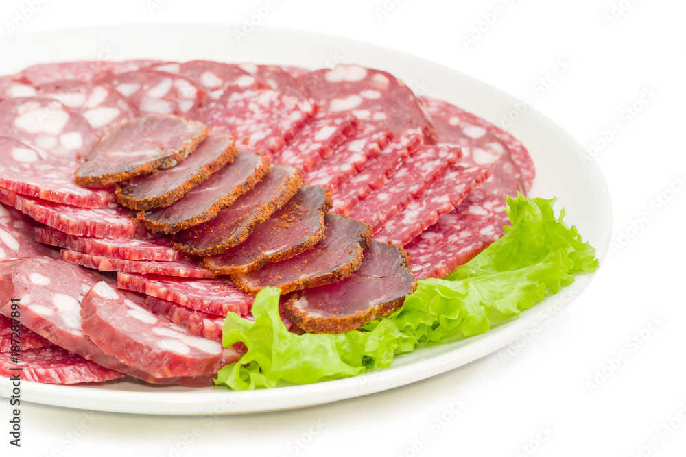 Sliced different meat products on lettuce on white dish closeup