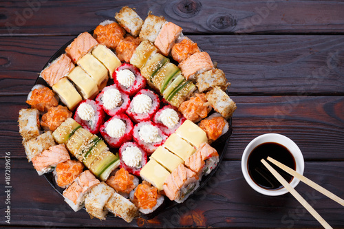 Tasty appetizing multicolored sushi rolls set, served with soy sauce and chopsticks on wooden table, view from above. Sushi restaurant concept