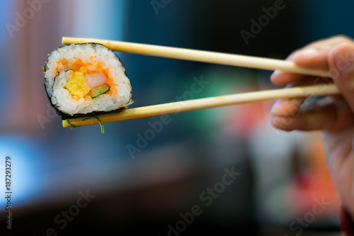 Sushi rolls holding by chopsticks in restaurant. Sushi is japanese food ,it is popular food in asia people.