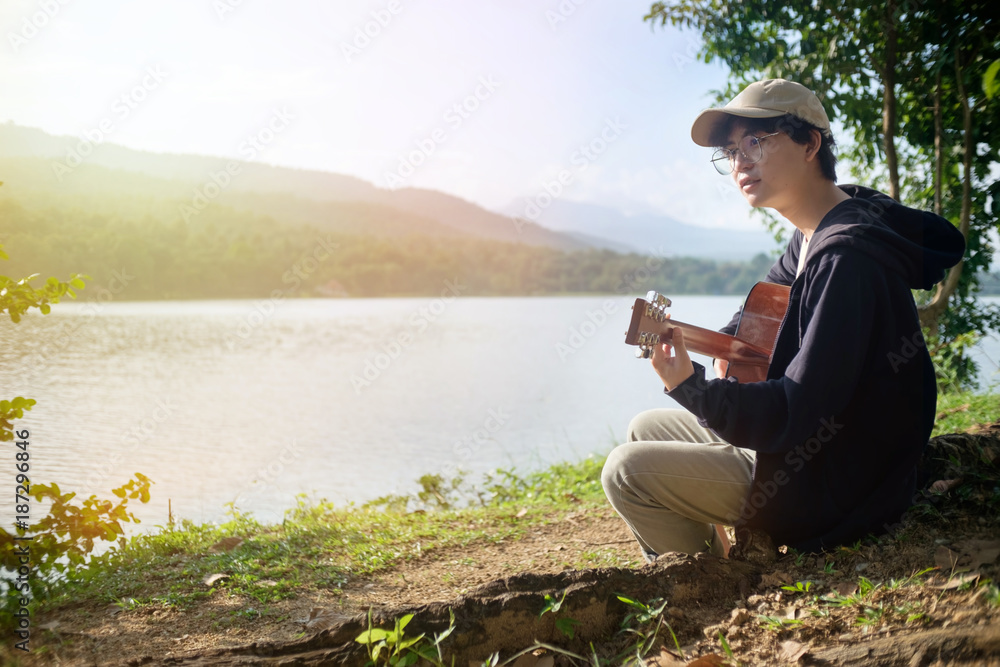 Man playing guitar on nature outdoor with lake and mountains view at holiday time.
