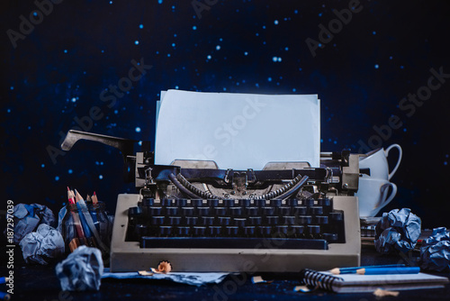 Modern typewriter with sheets of paper, empty coffee cups, pencils and notepads on a dark background. Editing and copywriting workplace. Creative writing concept. photo