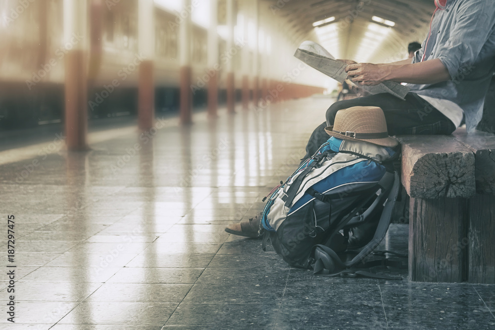 Obraz premium Travel concept,Backpack and hat at the train station A man sit with map.