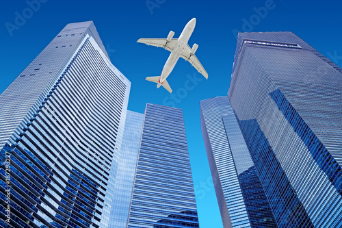 airplane flying in the blue sky over skyscrapers of a financial district
