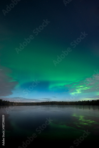 Northern Lights aka Aurora Borealis on midnight sky with reflections on the lake in Kurjenrahka National Park, Finland © Jamo Images