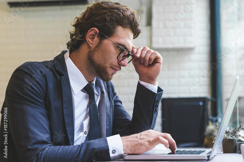 Handsome business man siting and using laptop computer. Male working in his workstation.