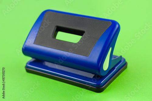 Single blue metal mechanical hole puncher on blank green paper