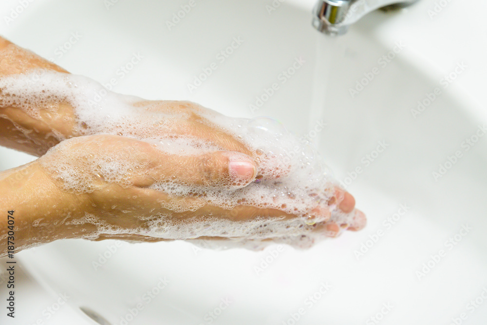 Fototapeta premium Closeup woman washing hands with soap under the faucet with water in the bathroom.