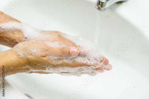 Closeup woman washing hands with soap under the faucet with water  in the bathroom.