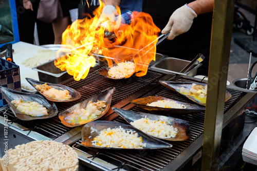 Photography Chopped fresh Atrina pectinata, with cheese on top, are cooked by a flamethrower