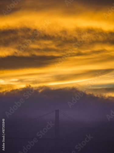 The outlines of Golden-Gate-Bridge shinig through a cloud during an amazing sunset in San Francisco, California